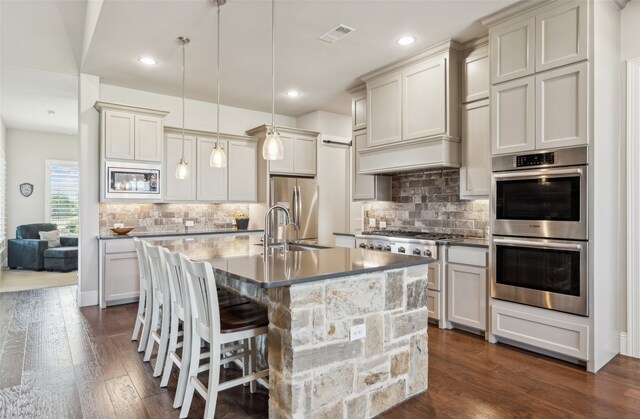 kitchen with a sink, a kitchen island with sink, stainless steel appliances, a kitchen bar, and dark wood finished floors