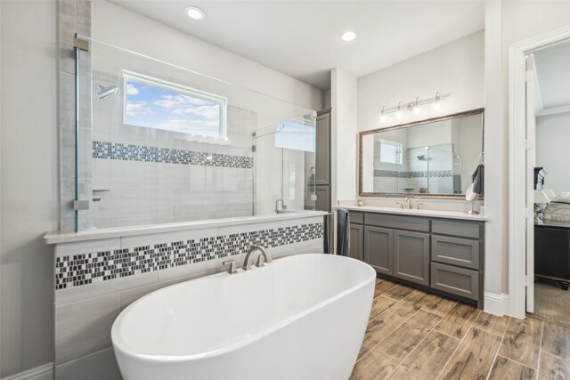 bathroom with recessed lighting, a shower stall, wood finished floors, vanity, and a freestanding tub