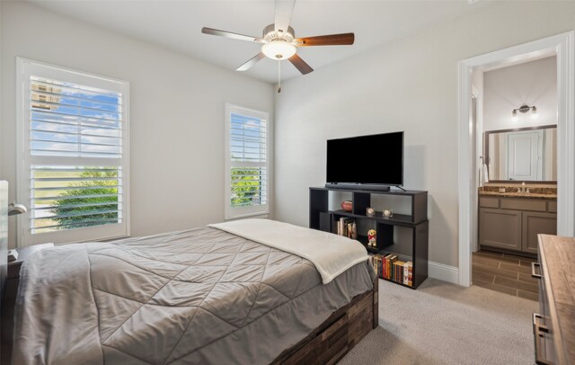 bedroom featuring a ceiling fan, light carpet, a sink, baseboards, and ensuite bathroom