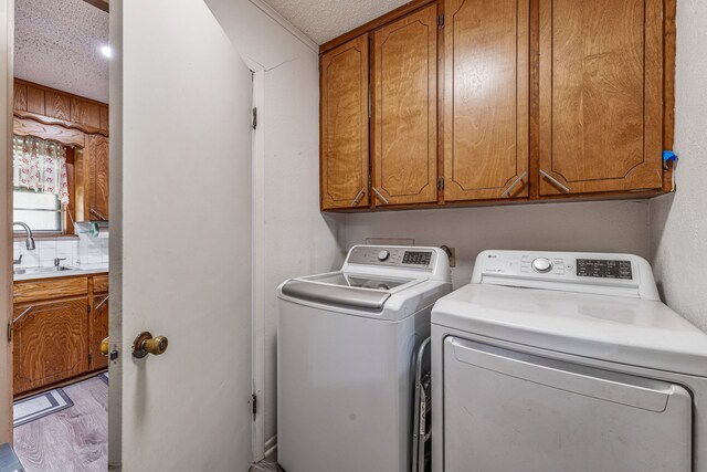 laundry area featuring light wood finished floors, washer and clothes dryer, a sink, cabinet space, and a textured ceiling