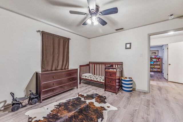 bedroom featuring a nursery area, wood finished floors, visible vents, and ceiling fan