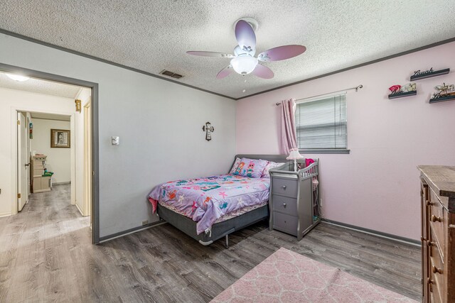 bedroom with ceiling fan, wood finished floors, visible vents, and a textured ceiling