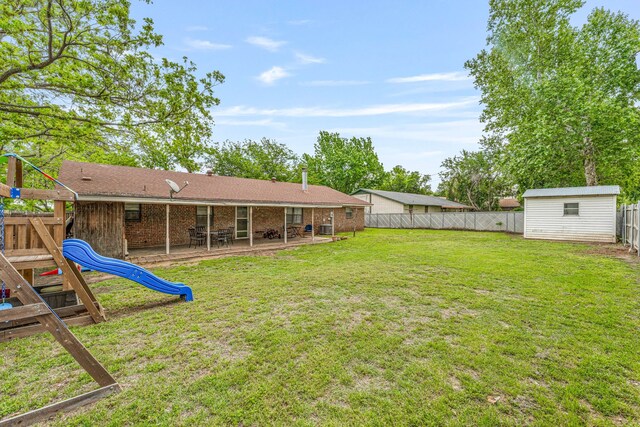 view of yard with an outbuilding, a fenced backyard, a playground, a shed, and a patio