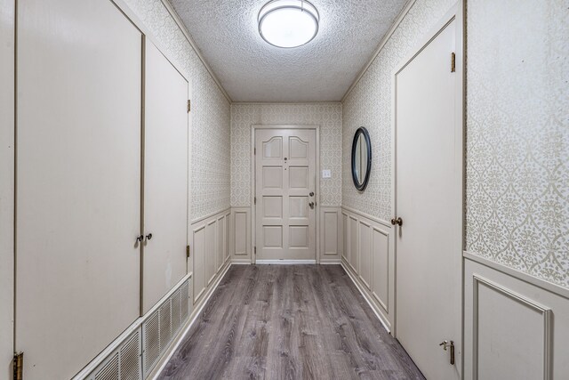 doorway to outside with wallpapered walls, wood finished floors, a textured ceiling, and a wainscoted wall