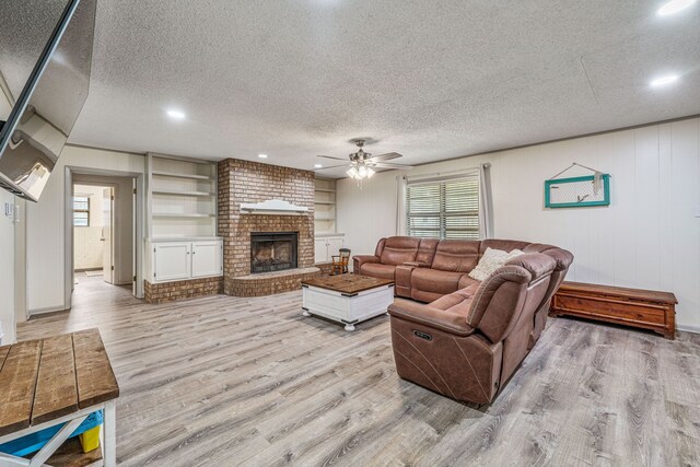 living area with recessed lighting, a textured ceiling, wood finished floors, a ceiling fan, and a brick fireplace