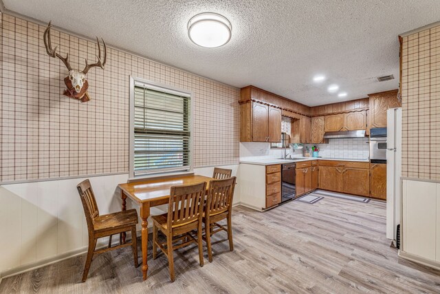 kitchen with a sink, a textured ceiling, dishwasher, light countertops, and under cabinet range hood