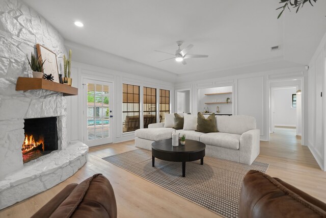 living area with a decorative wall, light wood-type flooring, a ceiling fan, and a high end fireplace