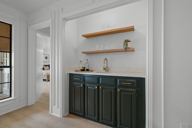bar featuring light wood-style floors, indoor wet bar, and a sink