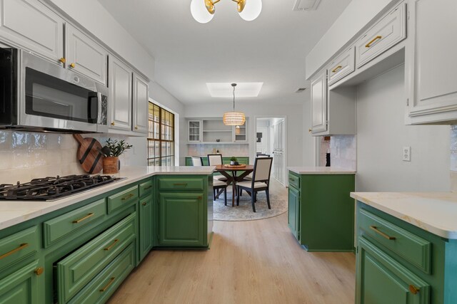 kitchen featuring stainless steel microwave, tasteful backsplash, white cabinetry, light countertops, and gas cooktop