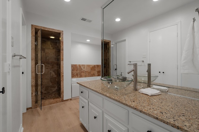 full bathroom featuring a shower stall, vanity, a bath, visible vents, and wood finished floors