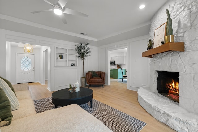 living room featuring a fireplace, ceiling fan, built in features, light wood-type flooring, and visible vents