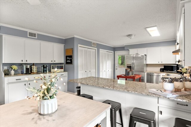 kitchen with visible vents, ornamental molding, a peninsula, a textured ceiling, and appliances with stainless steel finishes