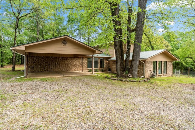 back of house featuring brick siding, a carport, driveway, and fence