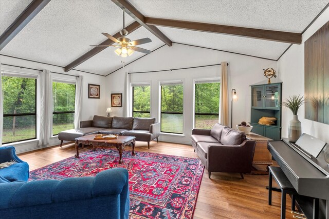 living room featuring a textured ceiling, light wood finished floors, a ceiling fan, and lofted ceiling with beams