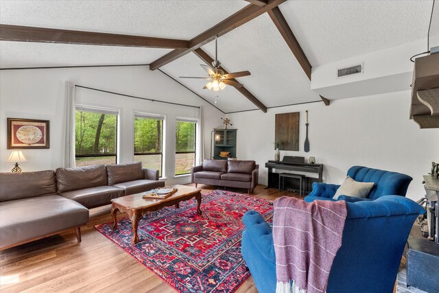 living area featuring lofted ceiling with beams, a textured ceiling, light wood-type flooring, visible vents, and ceiling fan