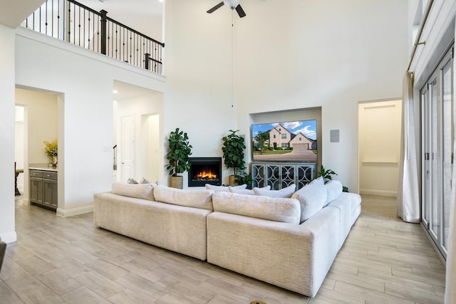 318 Waters Edge Dr, Argyle, TX 76226 - living area featuring a ceiling fan, a high ceiling, light wood-type flooring, a lit fireplace, and baseboards