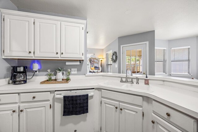 kitchen featuring white dishwasher, light countertops, white cabinetry, and a sink