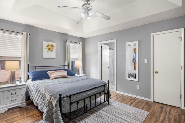 bedroom with baseboards, wood finished floors, a tray ceiling, and ceiling fan