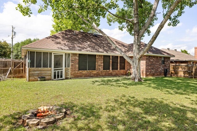 back of house with brick siding, a fenced backyard, a yard, a sunroom, and roof with shingles