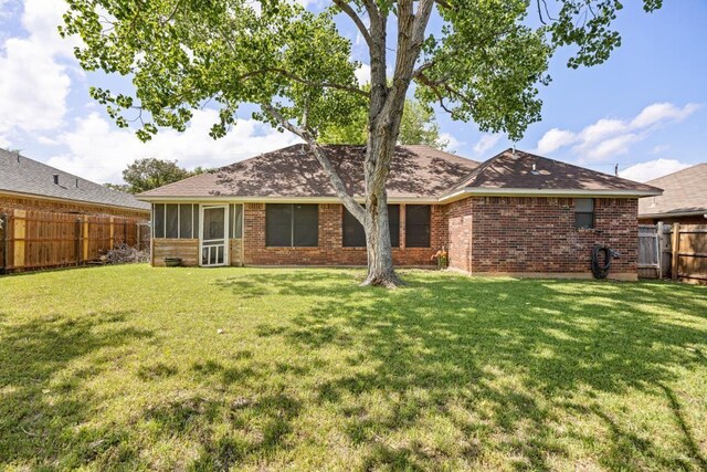 back of house featuring a fenced backyard, a sunroom, a yard, and roof with shingles