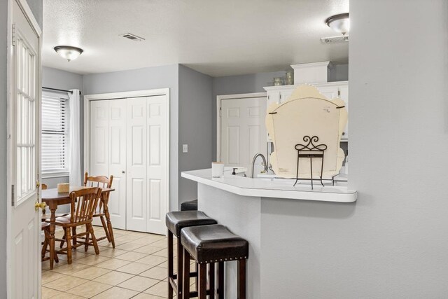kitchen with white cabinets, light countertops, visible vents, light tile patterned flooring, and a kitchen bar