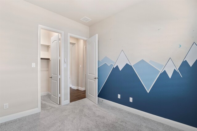 unfurnished bedroom with visible vents, a walk in closet, carpet floors, a closet, and baseboards