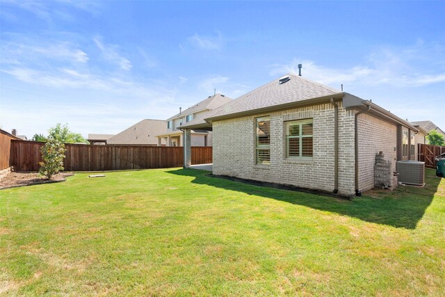 back of property with brick siding, central air condition unit, a fenced backyard, a yard, and roof with shingles