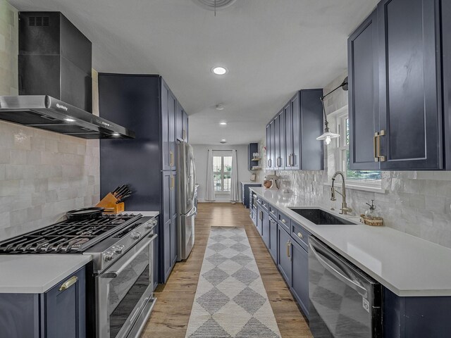 kitchen featuring wall chimney exhaust hood, stainless steel appliances, light wood-style flooring, and a sink