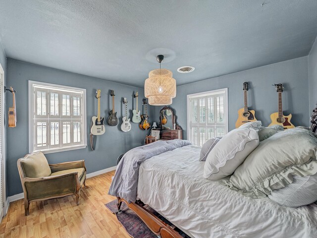 bedroom featuring a textured ceiling, visible vents, light wood finished floors, and baseboards