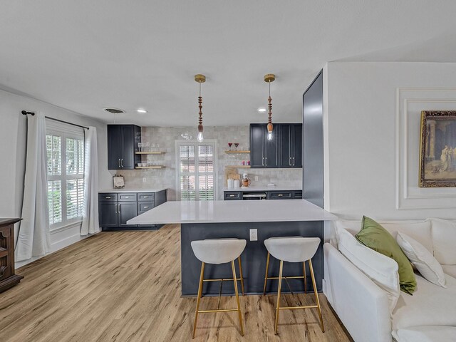 kitchen with light wood finished floors, a kitchen breakfast bar, backsplash, open shelves, and light countertops