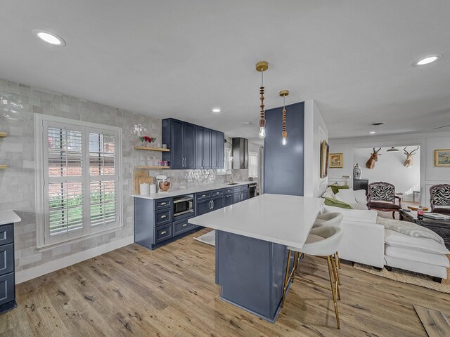 kitchen with blue cabinets, open floor plan, light countertops, a kitchen bar, and stainless steel microwave