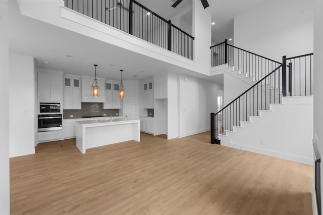 3541 Wardie Pl, Frisco, TX 75033 - kitchen with light wood-type flooring, a towering ceiling, open floor plan, and white cabinetry