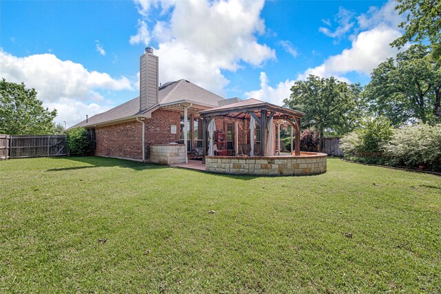 rear view of property featuring a fenced backyard, a gazebo, a chimney, brick siding, and a lawn