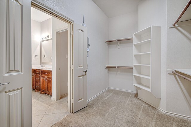 spacious closet featuring light tile patterned floors, a sink, and light colored carpet