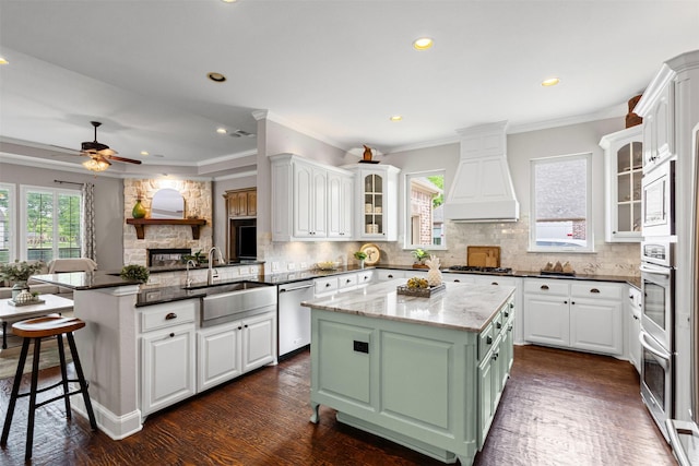 kitchen featuring custom exhaust hood, a sink, stainless steel appliances, a peninsula, and white cabinetry