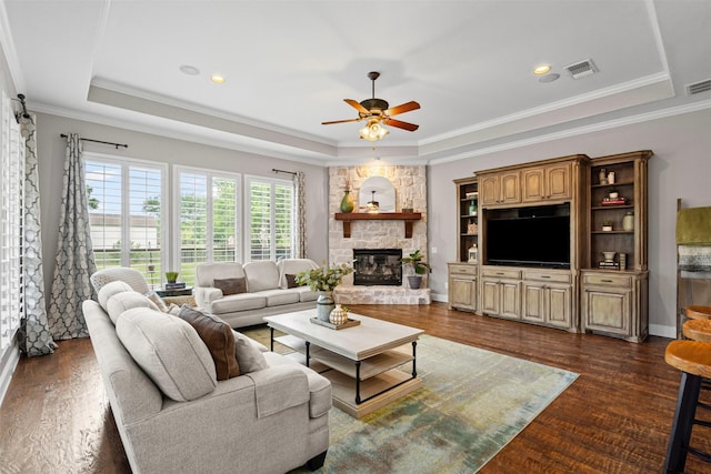 living area featuring dark wood-style floors, a tray ceiling, a stone fireplace, visible vents, and a ceiling fan
