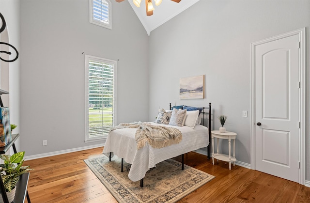 bedroom with light wood finished floors, a ceiling fan, baseboards, and high vaulted ceiling