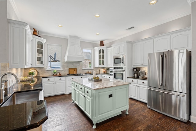 kitchen with custom exhaust hood, white cabinetry, appliances with stainless steel finishes, and visible vents