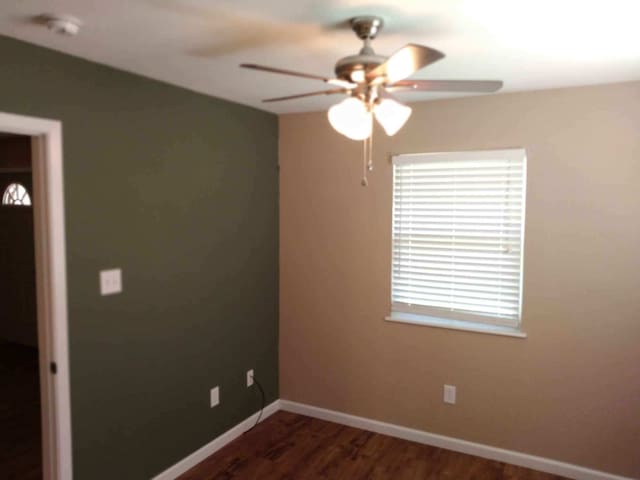 spare room featuring dark wood-style floors, ceiling fan, and baseboards