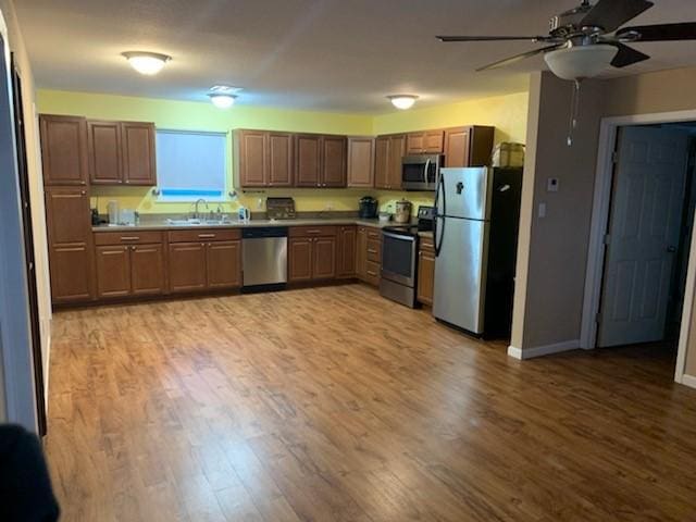 kitchen with light wood finished floors, a sink, ceiling fan, baseboards, and appliances with stainless steel finishes