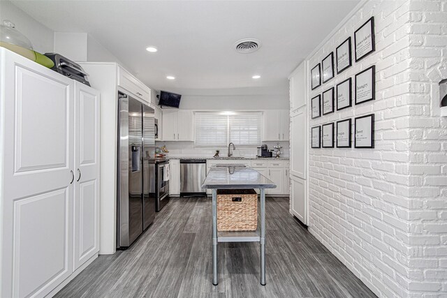 kitchen featuring a sink, brick wall, stainless steel appliances, white cabinetry, and dark wood-type flooring