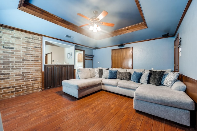 2307 Castle Rock Rd, Carrollton, TX 75007 - living area featuring a tray ceiling, a ceiling fan, wood-type flooring, brick wall, and ornamental molding