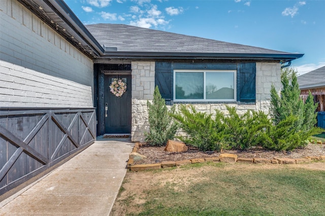 property entrance with stone siding, a lawn, and a shingled roof
