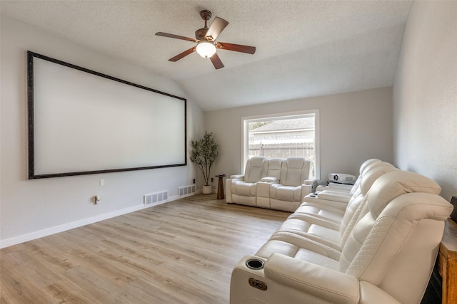 home theater room featuring vaulted ceiling, wood finished floors, visible vents, and a ceiling fan