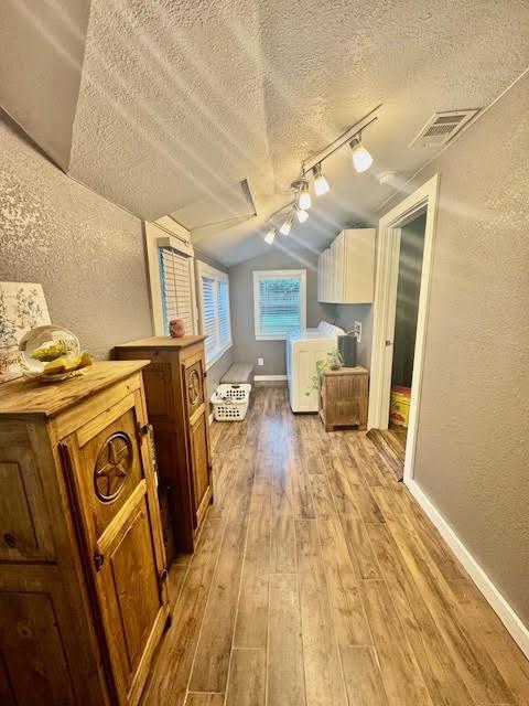715 W Ball St, Weatherford, TX 76086 - additional living space with washer and dryer, light wood finished floors, vaulted ceiling, a textured wall, and a textured ceiling