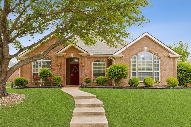 single story home with a front yard, a shingled roof, and brick siding