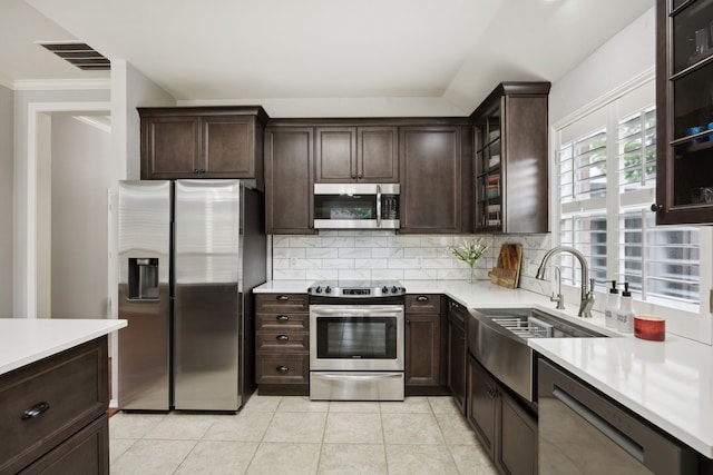 kitchen with a sink, dark brown cabinetry, backsplash, light countertops, and appliances with stainless steel finishes