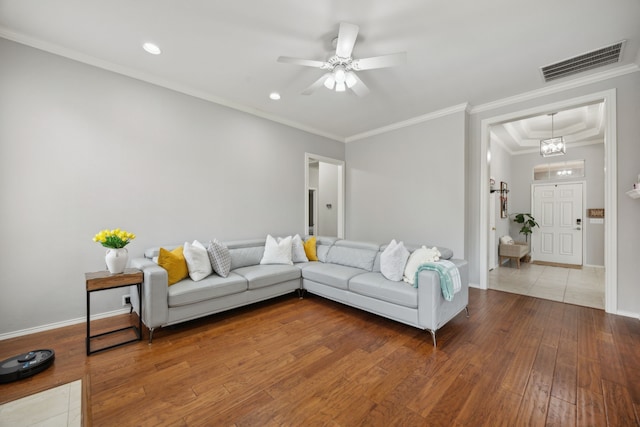 living area with a ceiling fan, hardwood / wood-style flooring, baseboards, ornamental molding, and visible vents