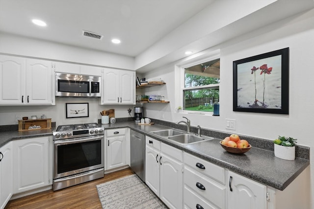 kitchen featuring stainless steel appliances, dark countertops, visible vents, and a sink
