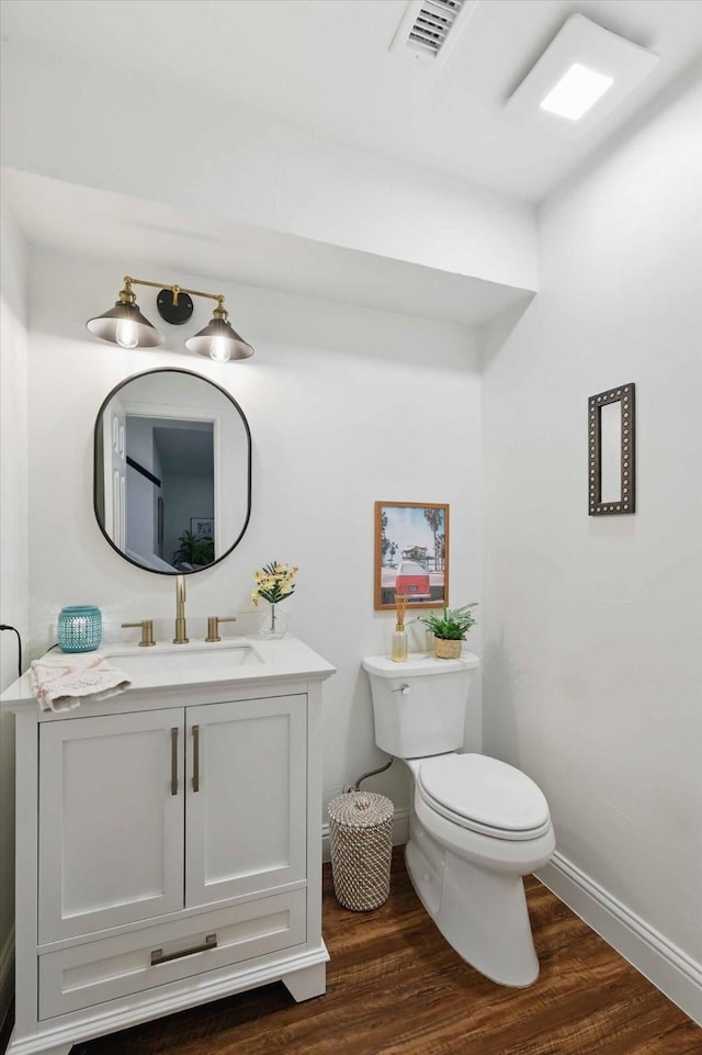 half bath with baseboards, toilet, wood finished floors, and visible vents
